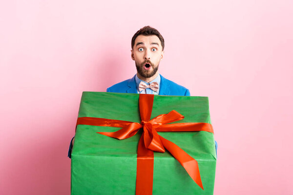 шокированный бородатый мужчина держит большую подарочную коробку на розовый
 