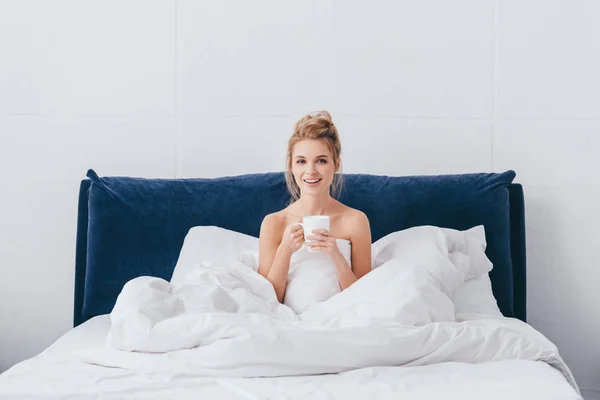 朝になるとベッドにコーヒーを飲みながら笑顔の女性が — ストック写真