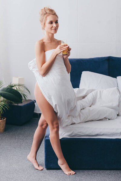 attractive naked woman with glass of juice in white sheets in bedroom in morning