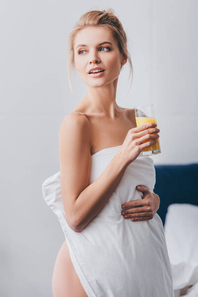 attractive woman with glass of juice in white sheets in bedroom in morning