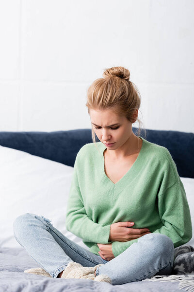 blonde woman having abdominal pain and sitting on bed