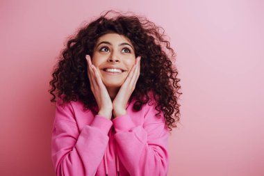Mutlu çift ırklı kız yüzüne dokunuyor ve pembe arka plana bakıyor.