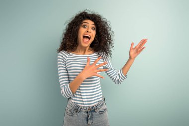 shocked mixed race girl pointing with hands while looking at camera on grey background clipart