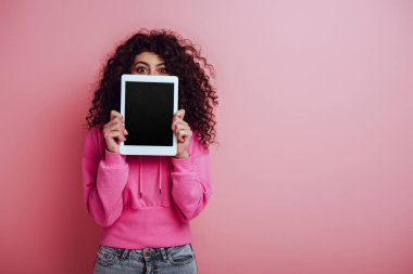  Pembe arka planda boş ekranlı dijital tablet gösteren çift ırklı kız