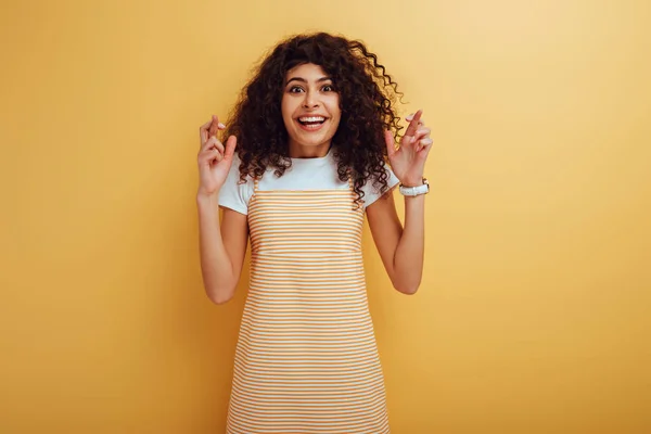 Excited Racial Girl Holding Crossed Fingers While Smiling Camera Yellow — Stock Photo, Image