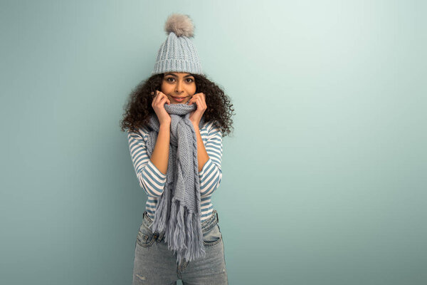 pretty bi-racial girl in warm hat and scarf smiling at camera on grey background