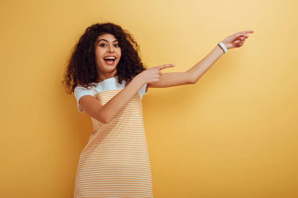 Vzrušená Rasová Dívka Ukazuje Prsty Při Pohledu Fotoaparát Žlutém Pozadí — Stock fotografie