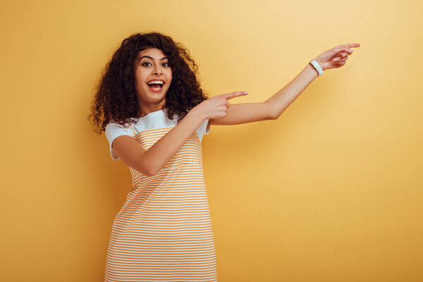 возбужденная двурасовая девушка, указывающая пальцами на камеру на желтом фоне
