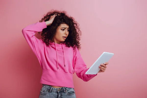 Rozczarowana Birasowa Dziewczyna Dotykająca Włosów Patrząc Cyfrową Tabletkę Różowym Tle — Zdjęcie stockowe