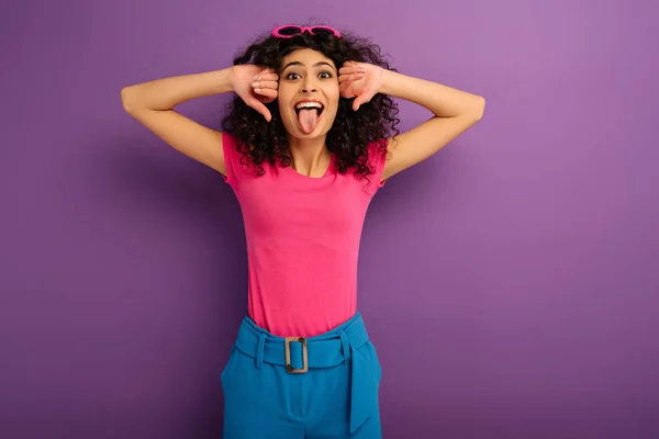 Alegre Racial Chica Sobresaliendo Lengua Mientras Mira Cámara Púrpura Fondo — Foto de Stock