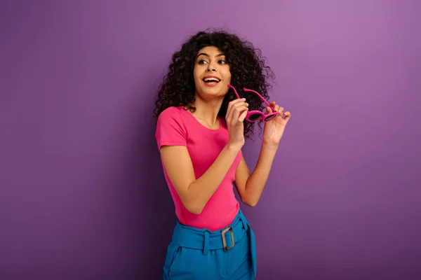 Sonriente Racial Chica Sosteniendo Gafas Sol Mientras Mira Hacia Otro — Foto de Stock