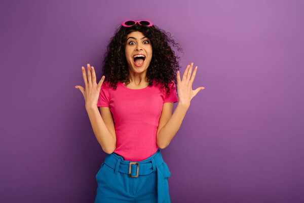 excited bi-racial girl showing wow gesture while looking at camera on purple background