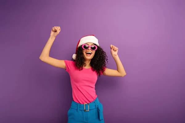 Веселая Двурасовая Девушка Шляпе Санты Солнечных Очках Танцует Фиолетовом Фоне — стоковое фото