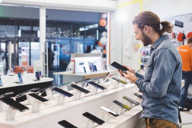 Ev aletleri mağazasında elinde akıllı telefon tutan gülümseyen adamın yan görüntüsü 
