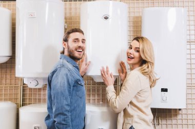smiling boyfriend and girlfriend touching boiler in home appliance store  clipart