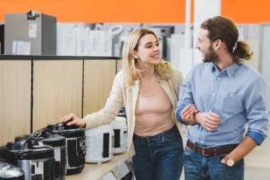 smiling consultant and woman talking near slow cookers in home appliance store  clipart
