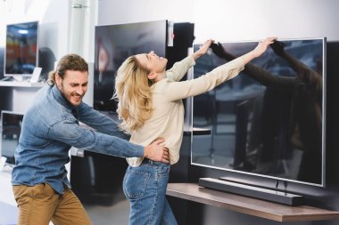 angry boyfriend pulling girlfriend with tv in home appliance store  clipart