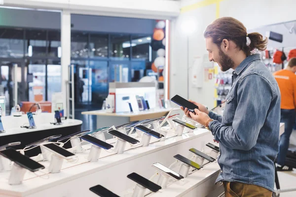 微笑的男人在家用电器商店里拿着智能手机的侧面视图 — 图库照片