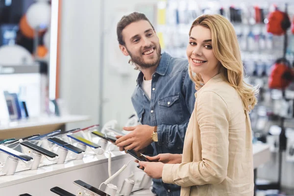 微笑的男女朋友在家用电器商店里拿着新的智能手机 — 图库照片