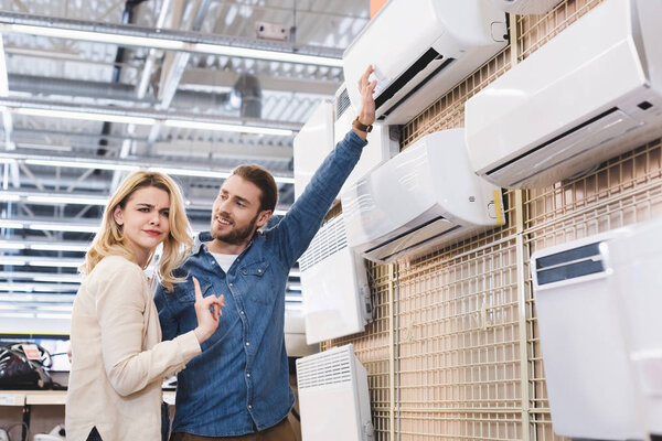 boyfriend pointing with hand at air conditioner and girlfriend showing no gesture in home appliance store 