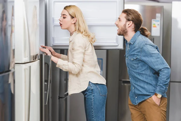 side view of shocked boyfriend and girlfriend looking at fridge in home appliance store
