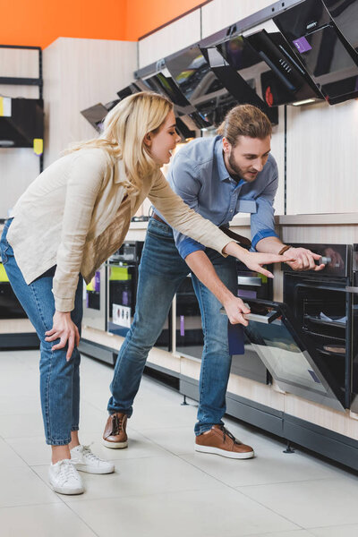 consultant use oven and smiling woman pointing with hand in home appliance store 