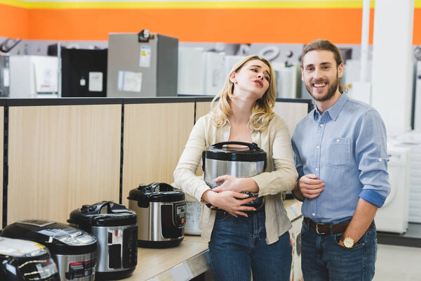 woman holding slow cooker and talking with smiling consultant in home appliance store 