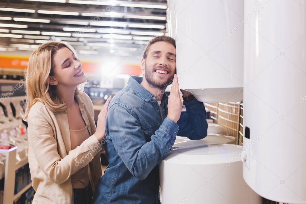 smiling boyfriend touching boiler and girlfriend looking at him in home appliance store 