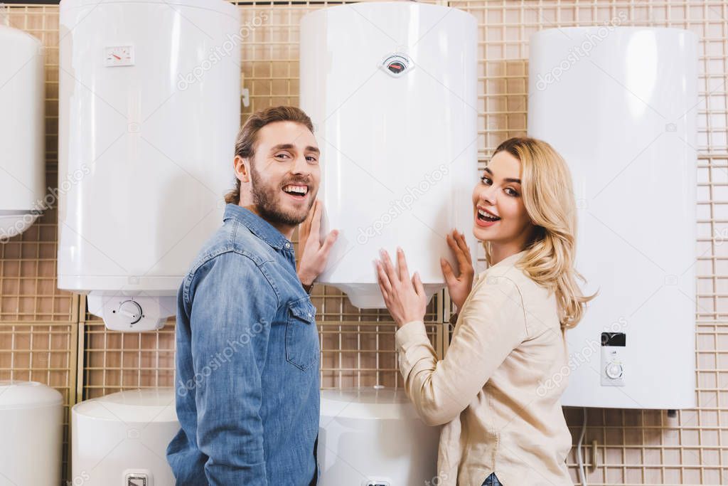 smiling boyfriend and girlfriend touching boiler in home appliance store 