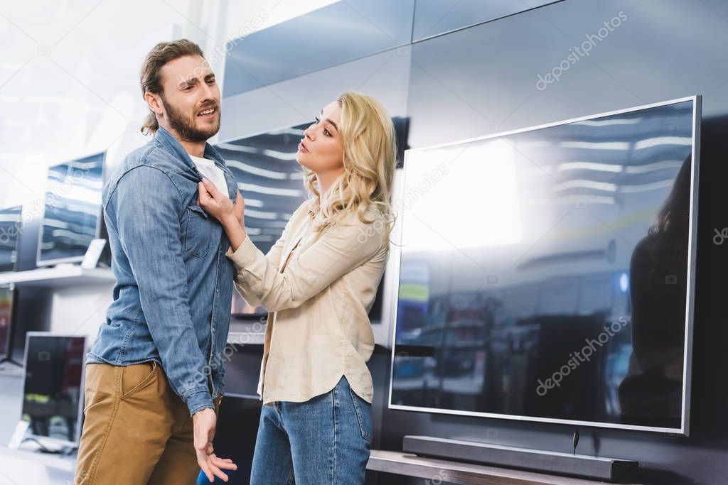 girlfriend asking sad boyfriend near tv in home appliance store 