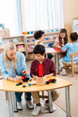 Montessori okulunda arka planda çocukları olan bir öğretmen tarafından yapı blokları oynanıyor.