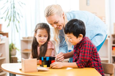 Gülümseyen öğretmen Montessori dersinde çocuklarla yapı taşı oynuyor. 