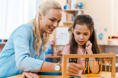 Gülümseyen öğretmen ve çocuk Montessori sınıfında masada ahşap oyun oynuyorlar.