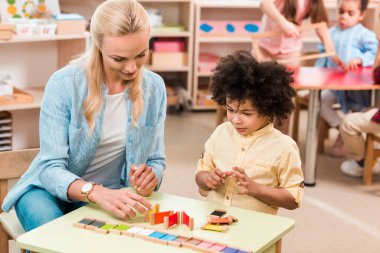 Montessori okulunda çocuklu bir öğretmenin ahşap oyunu oynaması üzerine seçici bir odaklanma.