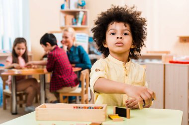 Tahta oyunu olan Afrikalı Amerikalı çocuğun seçici odak noktası ve Montessori okulunda çocuklu öğretmen.