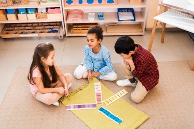 Montessori sınıfında yerde oturmuş oyun oynayan çocukların yüksek açılı görüntüsü