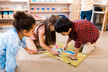 Montessori sınıfında yerde oturan çocuklar eğitim oyunu oynuyorlar. 