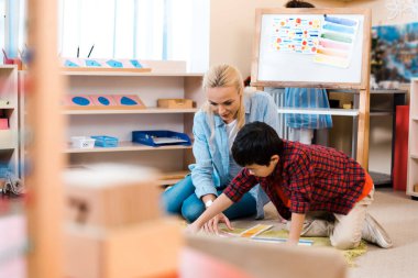 Montessori okulunda öğrenciyle oynayan öğretmenin seçici odağı