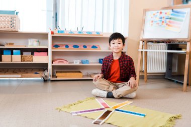 Gülümseyen Asyalı çocuk Montessori okulunda yerde eğitime dayalı kameraya bakıyor.