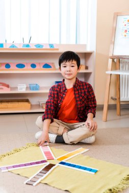 Montessori okulunda yerde eğitim oyunu oynarken kameraya bakan çocuk
