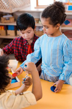 Montessori okulunda ders sırasında kum saati ve masa oyunu oynayan çocukların seçici odak noktası