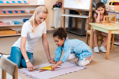 Montessori okulunda öğretmenlerin seçmeli odak noktası, yerde oynayan çocuk ve masada oturan sıkıcı çocuk.