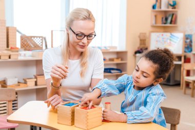 Öğretmen ve çocuk Montessori okulunda masa başında tahta oyunu oynuyorlar.