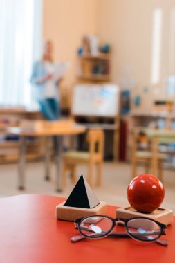 Montessori okulunda öğretmenle birlikte eğitim oyunu ve gözlüklerin seçici odak noktası masada.