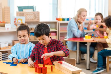 Montessori okulunda çocuklarla ve öğretmenle oyun oynayan çocukların seçici odak noktası 