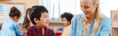 Montessori okulunda gülümseyen öğretmen ve çocuklu bir çocuğun panoramik fotoğrafı.