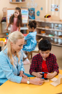 Montessori sınıfında çocuklarla yapı taşı oynayan öğretmen ve çocuğun seçici odak noktası 
