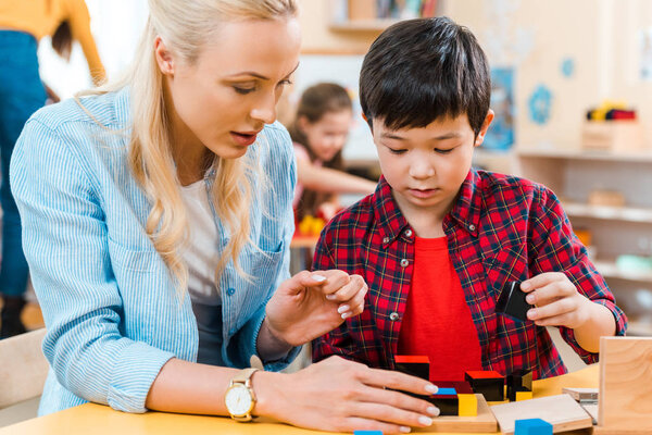 Selective focus of teacher and child playing building blocks with kids at background in montessori school