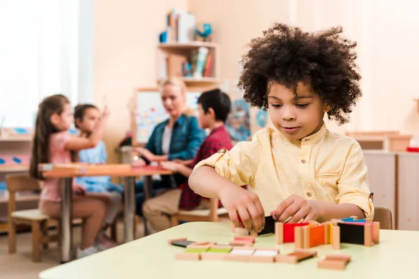 Montessori okulunda öğretmen ve çocuklarla eğitim oyunu oynayan Afrikalı Amerikalı çocuğun seçici odak noktası