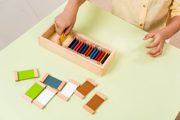 Cropped view of kid playing educational game with colorful boards at table in montessori school